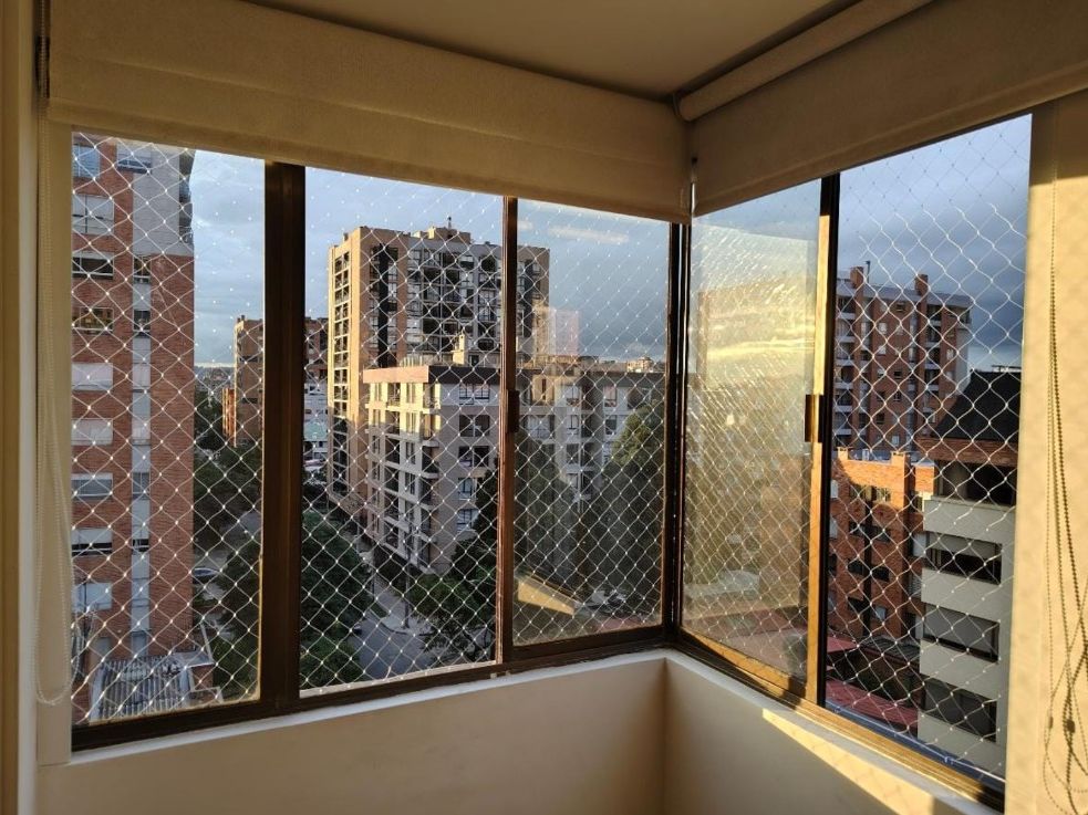 Vista interior de ventanas de departamento con malla romboidal y edificios al fondo