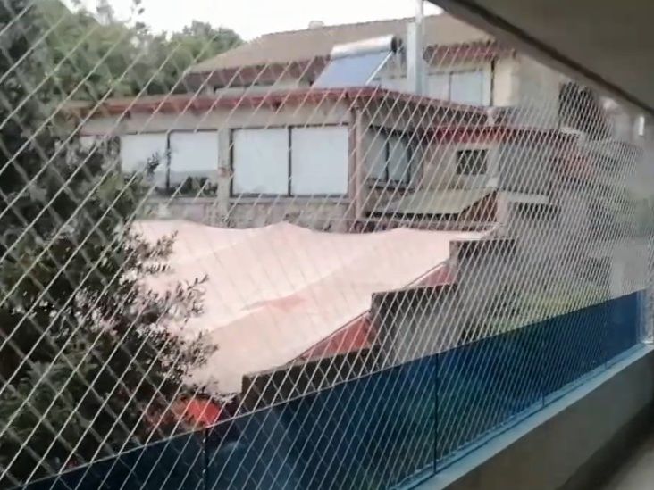 Malla romboidal de seguridad cerrando el frente de un balcón, con vista a casas y árboles